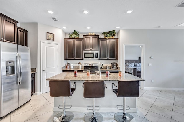 kitchen with light stone counters, stainless steel appliances, a breakfast bar, and a kitchen island with sink