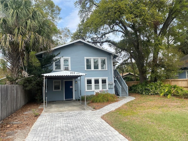 traditional home with stairway, decorative driveway, a front yard, and fence