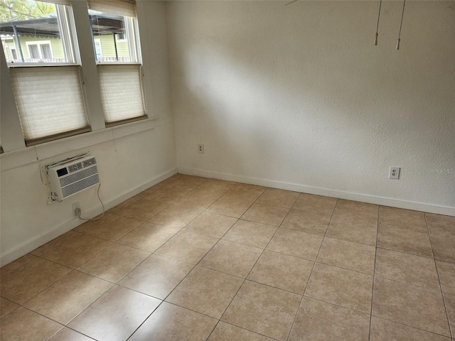 spare room with light tile patterned floors, an AC wall unit, and baseboards