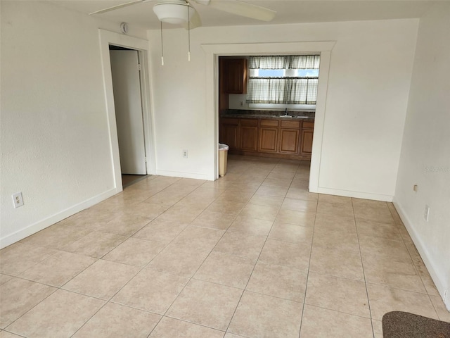 spare room with light tile patterned floors, baseboards, ceiling fan, and a sink