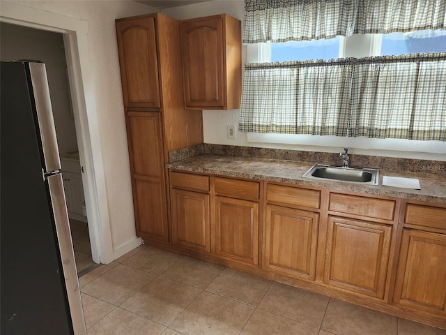 kitchen featuring a sink, light tile patterned flooring, brown cabinetry, and freestanding refrigerator