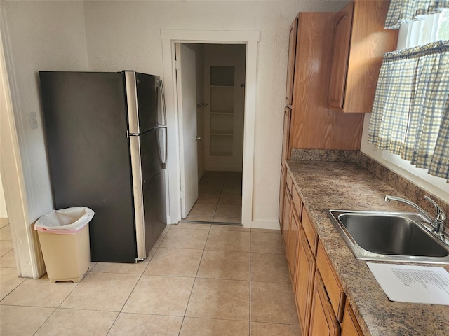 kitchen featuring light tile patterned floors, freestanding refrigerator, a sink, a textured wall, and brown cabinets