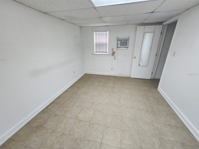 spare room featuring a drop ceiling, baseboards, and a wall unit AC