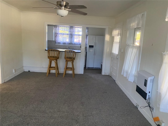 interior space with heating unit, a ceiling fan, dark carpet, and ornamental molding