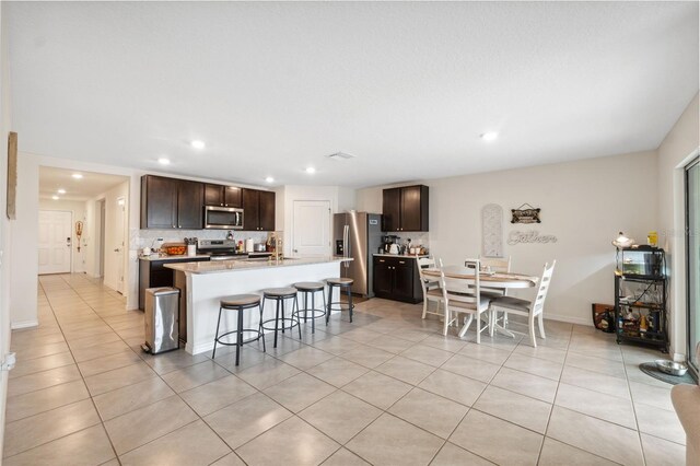 kitchen featuring dark brown cabinetry, appliances with stainless steel finishes, a breakfast bar, and a center island with sink