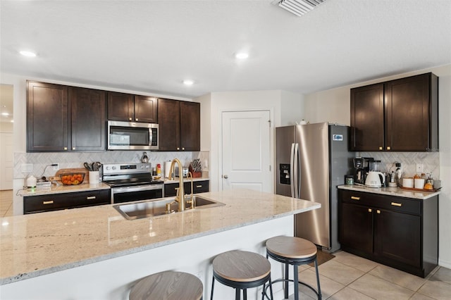 kitchen with light stone countertops, appliances with stainless steel finishes, dark brown cabinets, and sink