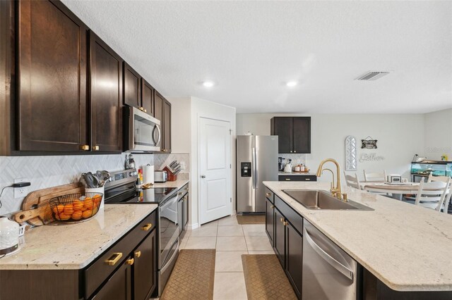 kitchen with sink, appliances with stainless steel finishes, backsplash, an island with sink, and light tile patterned flooring