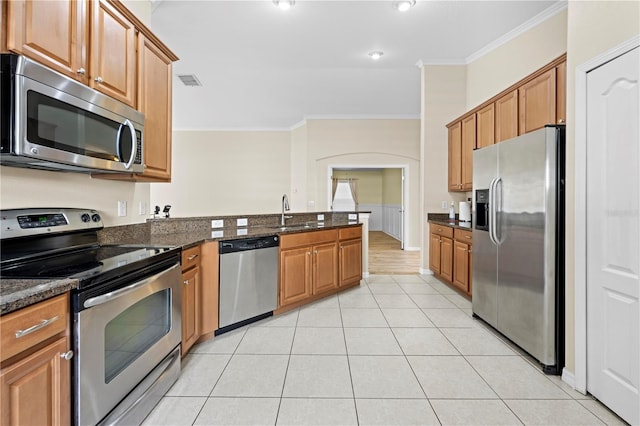 kitchen with appliances with stainless steel finishes, sink, dark stone countertops, light tile patterned floors, and crown molding