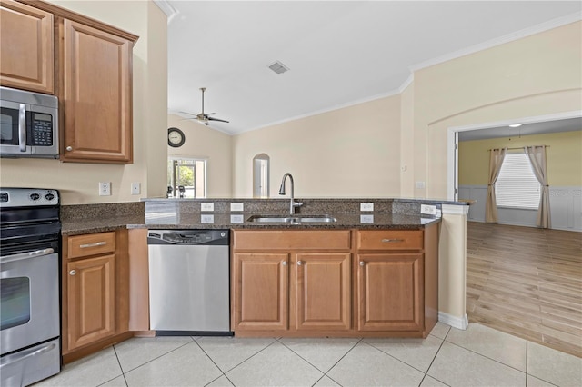 kitchen featuring sink, ornamental molding, appliances with stainless steel finishes, kitchen peninsula, and dark stone counters