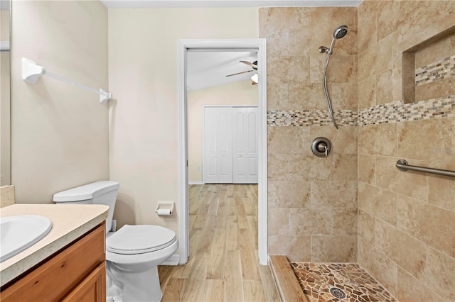 bathroom with lofted ceiling, toilet, wood-type flooring, a tile shower, and vanity