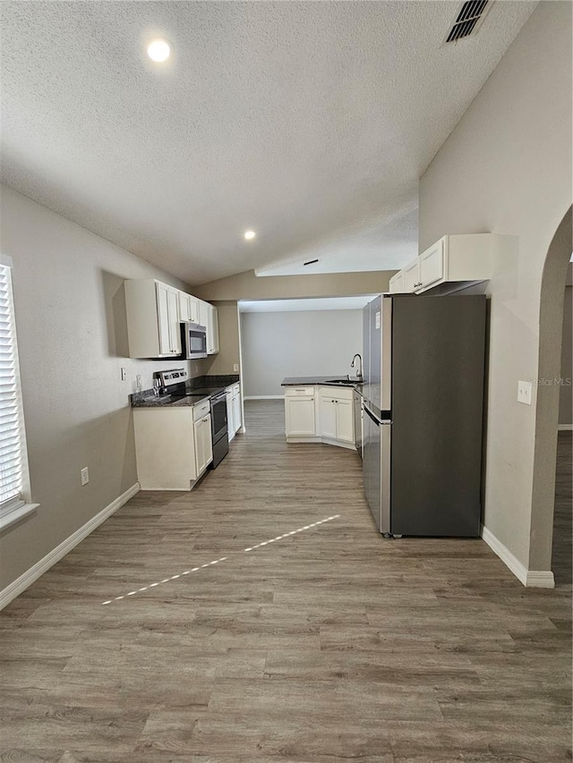 kitchen featuring lofted ceiling, appliances with stainless steel finishes, white cabinetry, a textured ceiling, and light wood-type flooring