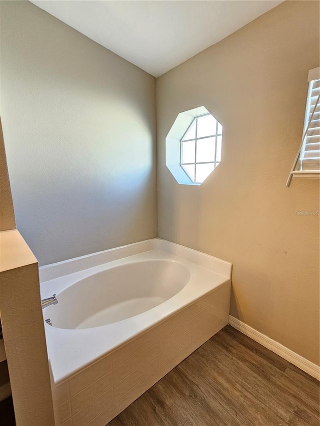 bathroom with a relaxing tiled tub and hardwood / wood-style flooring