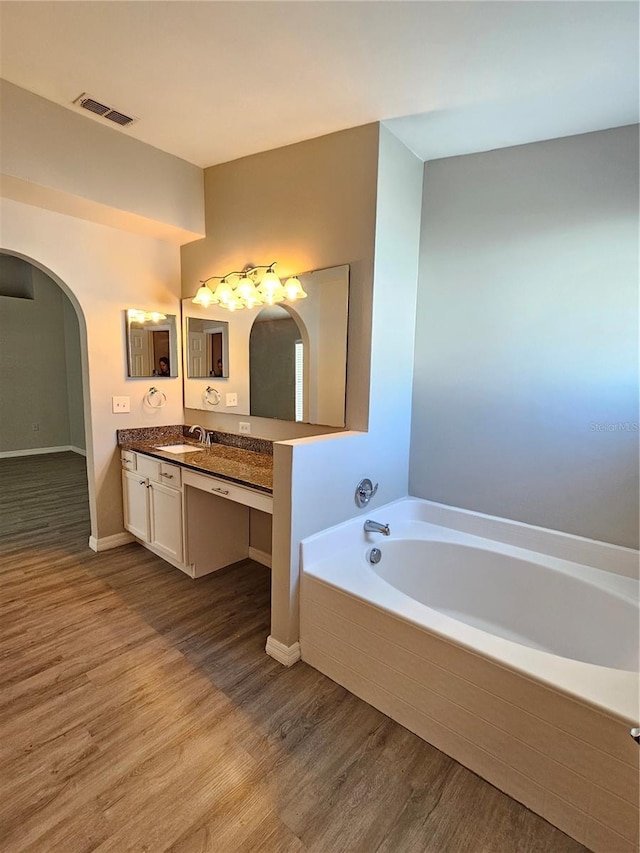 bathroom with hardwood / wood-style floors, vanity, and a relaxing tiled tub