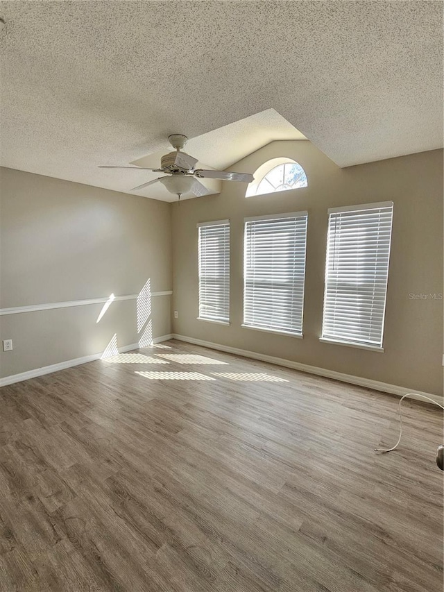 empty room with hardwood / wood-style flooring, ceiling fan, vaulted ceiling, and a textured ceiling