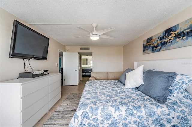 bedroom featuring ceiling fan, ensuite bath, a textured ceiling, and light tile patterned flooring