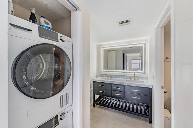 laundry area with stacked washing maching and dryer, sink, a textured ceiling, and light tile patterned floors