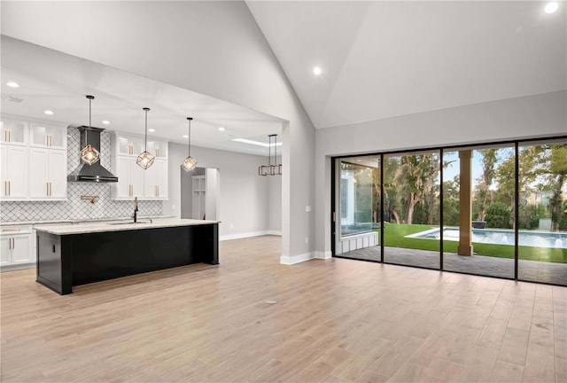 kitchen with white cabinetry, wall chimney range hood, hanging light fixtures, and a center island with sink