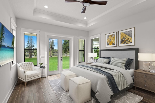 bedroom featuring wood-type flooring, a raised ceiling, multiple windows, and access to outside