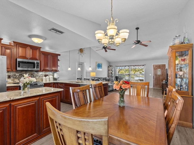 dining space with vaulted ceiling, sink, ceiling fan with notable chandelier, and light hardwood / wood-style floors