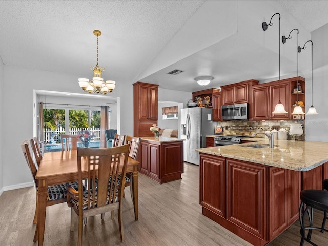 kitchen featuring vaulted ceiling, appliances with stainless steel finishes, kitchen peninsula, pendant lighting, and light hardwood / wood-style floors