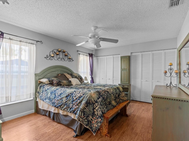 bedroom featuring hardwood / wood-style floors, two closets, a textured ceiling, and ceiling fan