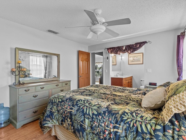 bedroom with sink, light hardwood / wood-style flooring, ceiling fan, ensuite bathroom, and a textured ceiling