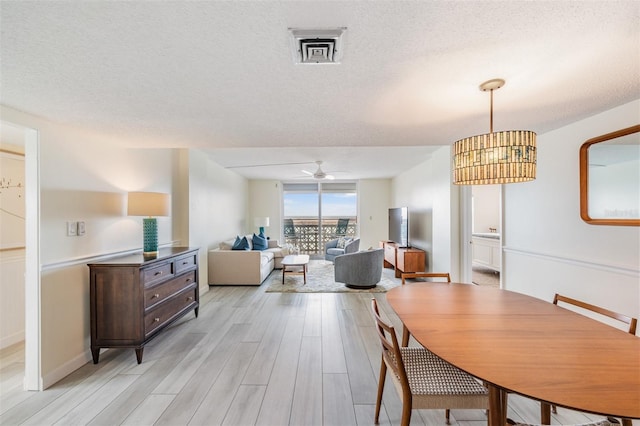 dining room featuring ceiling fan with notable chandelier, a textured ceiling, and light wood-type flooring