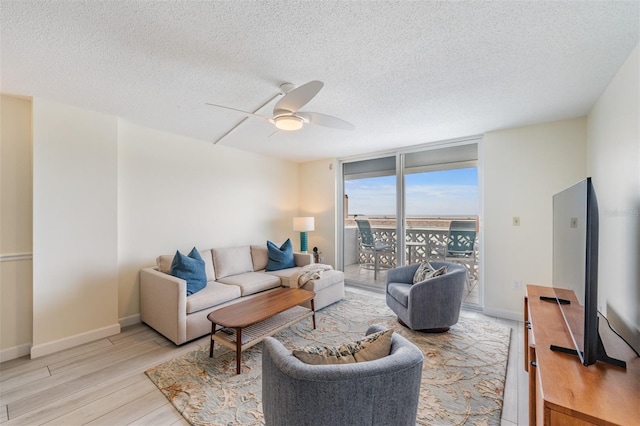 living room featuring ceiling fan, a textured ceiling, light wood-type flooring, and a wall of windows