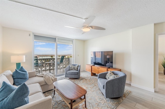 living room with ceiling fan, a textured ceiling, light wood-type flooring, and a wall of windows