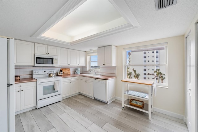 kitchen featuring white cabinetry, a textured ceiling, a tray ceiling, white appliances, and decorative backsplash