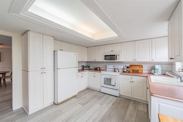 kitchen with white cabinetry, sink, white appliances, and a tray ceiling