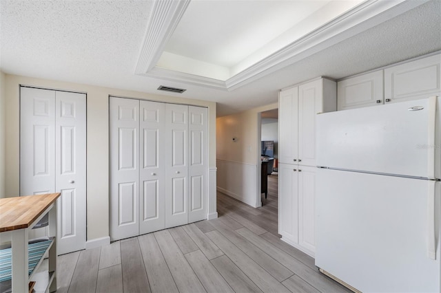 kitchen featuring light hardwood / wood-style flooring, white cabinetry, white refrigerator, a tray ceiling, and a textured ceiling