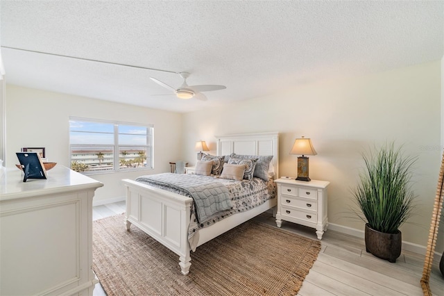 bedroom with ceiling fan, light hardwood / wood-style flooring, and a textured ceiling