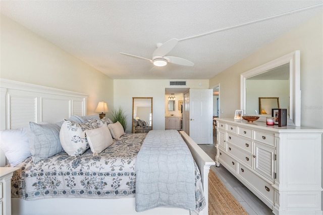 bedroom with ceiling fan, ensuite bath, and a textured ceiling