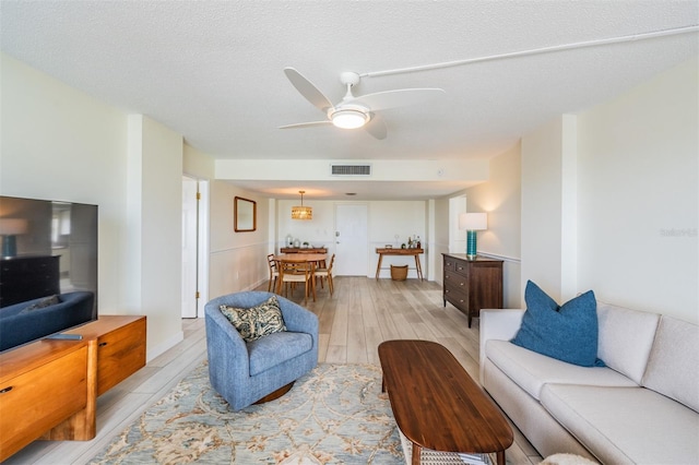 living room featuring ceiling fan, light hardwood / wood-style floors, and a textured ceiling