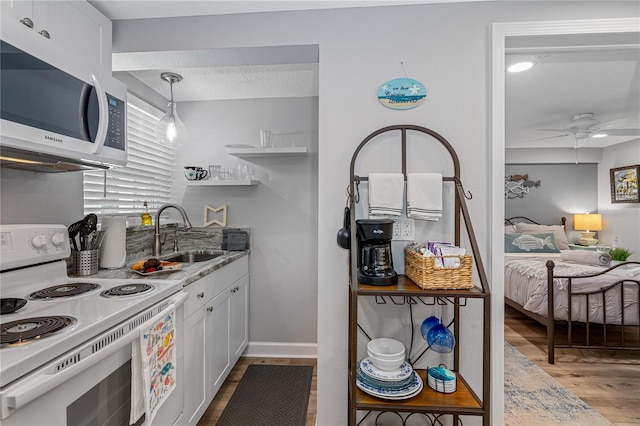 kitchen featuring sink, white range with electric stovetop, light stone counters, white cabinets, and decorative light fixtures