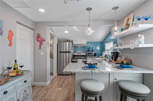 kitchen featuring sink, appliances with stainless steel finishes, a kitchen bar, kitchen peninsula, and light wood-type flooring