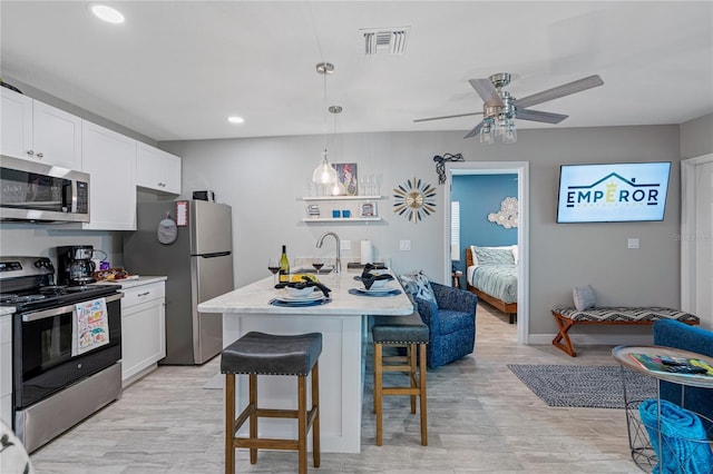 kitchen with pendant lighting, an island with sink, a breakfast bar area, white cabinets, and stainless steel appliances