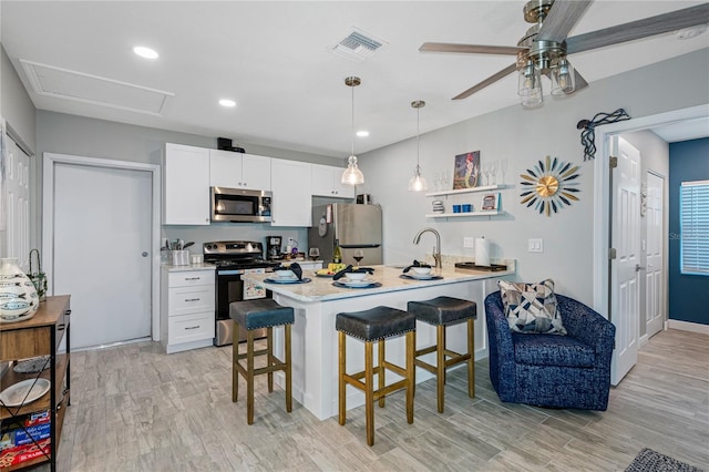 kitchen featuring light hardwood / wood-style flooring, appliances with stainless steel finishes, white cabinetry, a kitchen breakfast bar, and kitchen peninsula