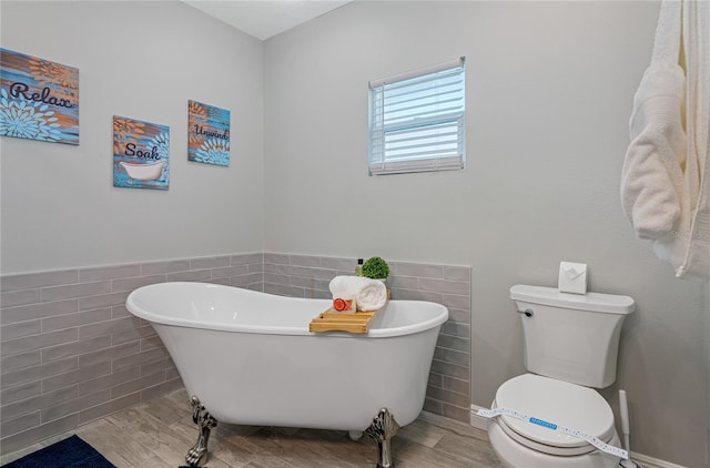 bathroom with tile walls, a tub to relax in, hardwood / wood-style floors, and toilet