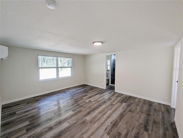 unfurnished room featuring dark wood-type flooring, a wall unit AC, and a textured ceiling