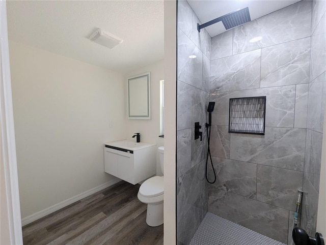 bathroom with a tile shower, vanity, hardwood / wood-style floors, and toilet