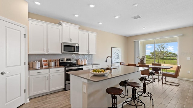 kitchen with a kitchen bar, sink, white cabinetry, stainless steel appliances, and a kitchen island with sink