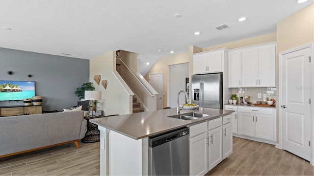 kitchen featuring sink, white cabinetry, appliances with stainless steel finishes, an island with sink, and backsplash