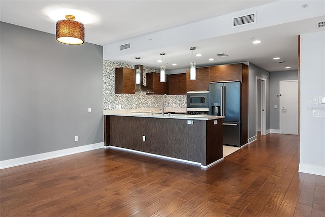 kitchen featuring hardwood / wood-style floors, high end fridge, kitchen peninsula, dark brown cabinets, and wall chimney range hood