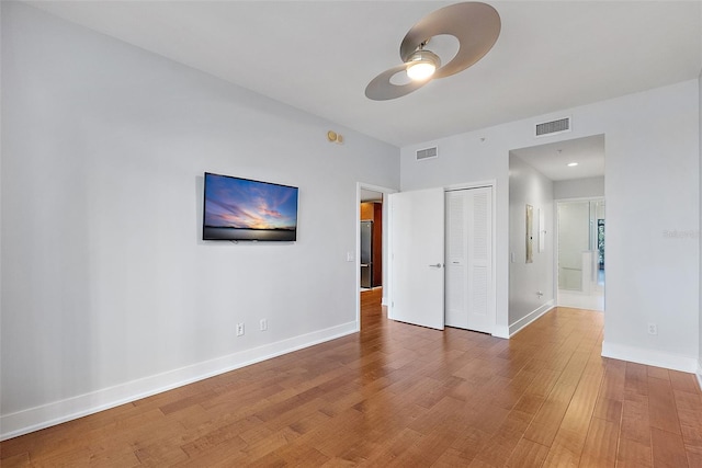 unfurnished bedroom with hardwood / wood-style floors, stainless steel fridge, ceiling fan, and a closet