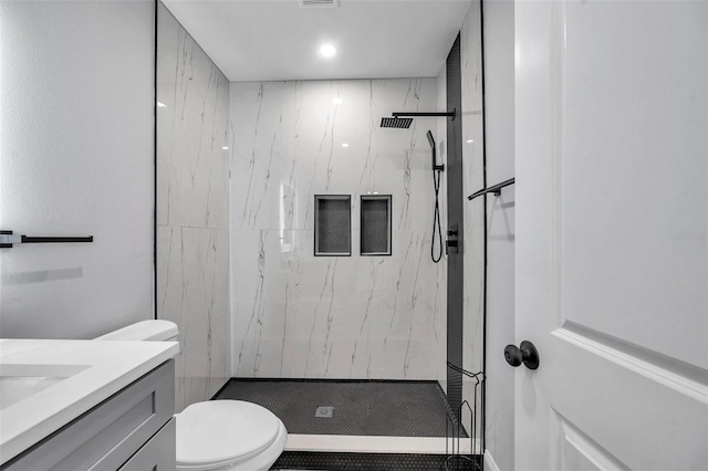 bathroom with a tile shower, vanity, and toilet