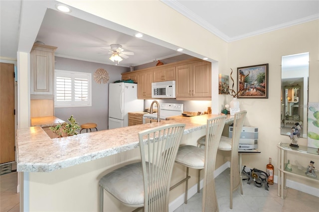 kitchen with white appliances, a kitchen breakfast bar, kitchen peninsula, and light brown cabinetry