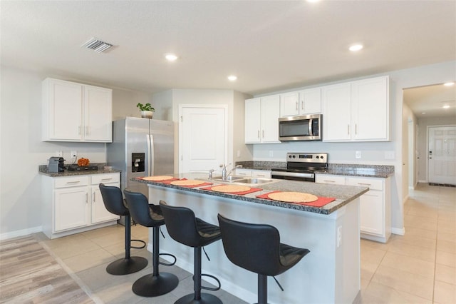 kitchen featuring stainless steel appliances, white cabinetry, a breakfast bar, and a center island with sink