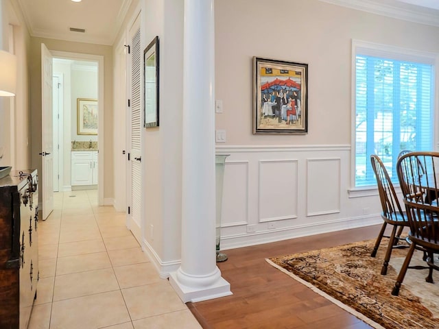 hallway featuring crown molding, decorative columns, and light wood-type flooring